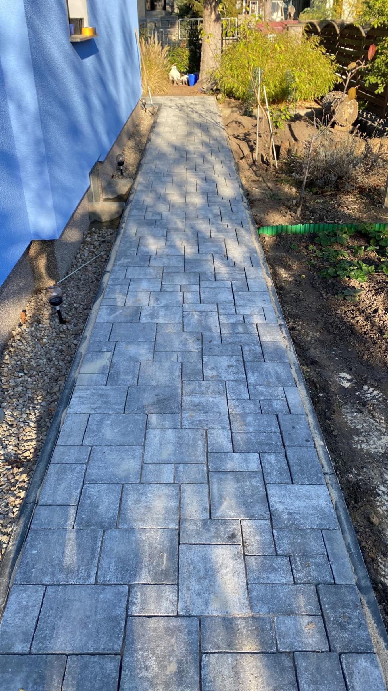 Seitlicher Pflasterweg entlang einer blauen Hauswand